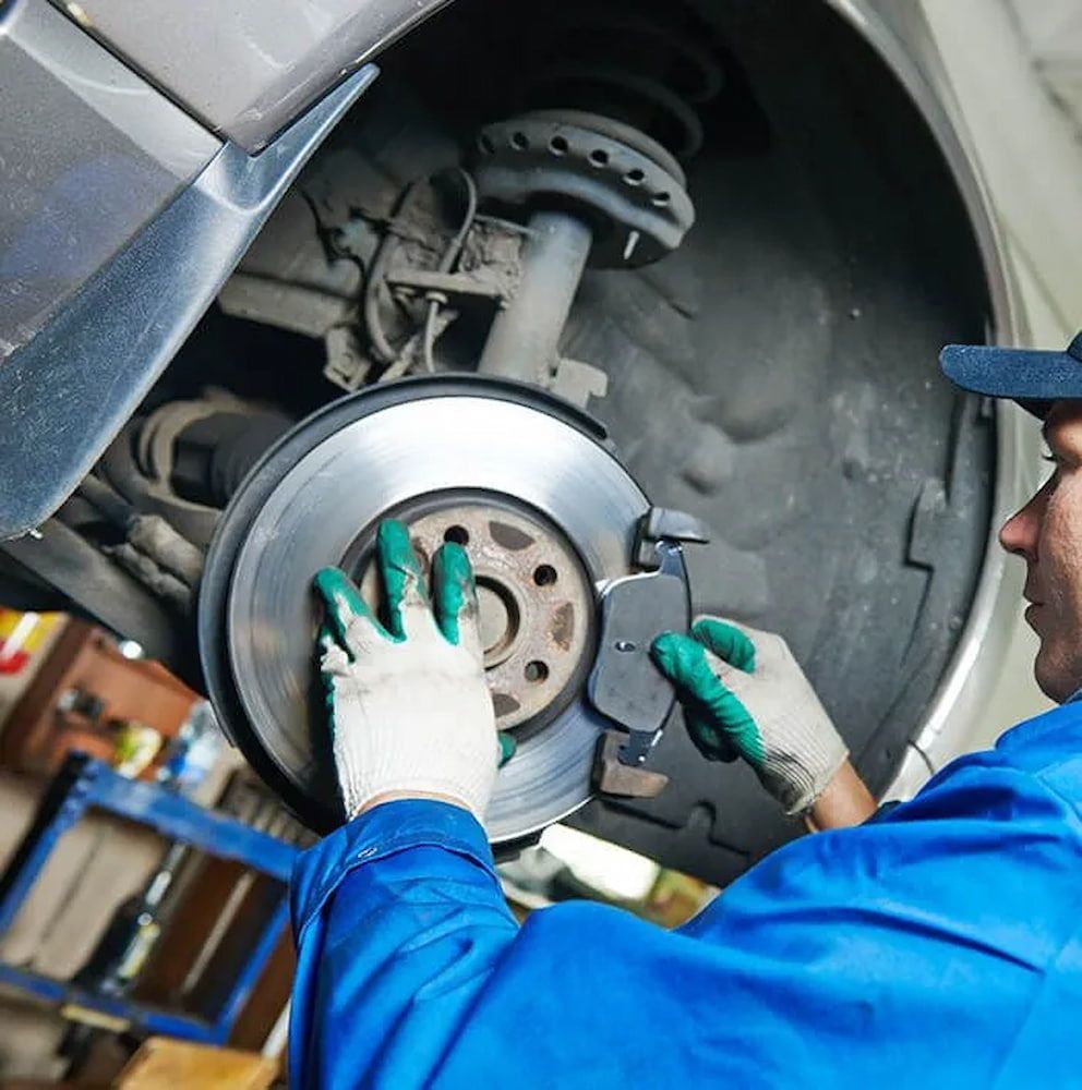 A Man Wearing Green Gloves Is Working On The Brake Pads Of A Car — Figtree Brake and Clutch in Figtree, NSW