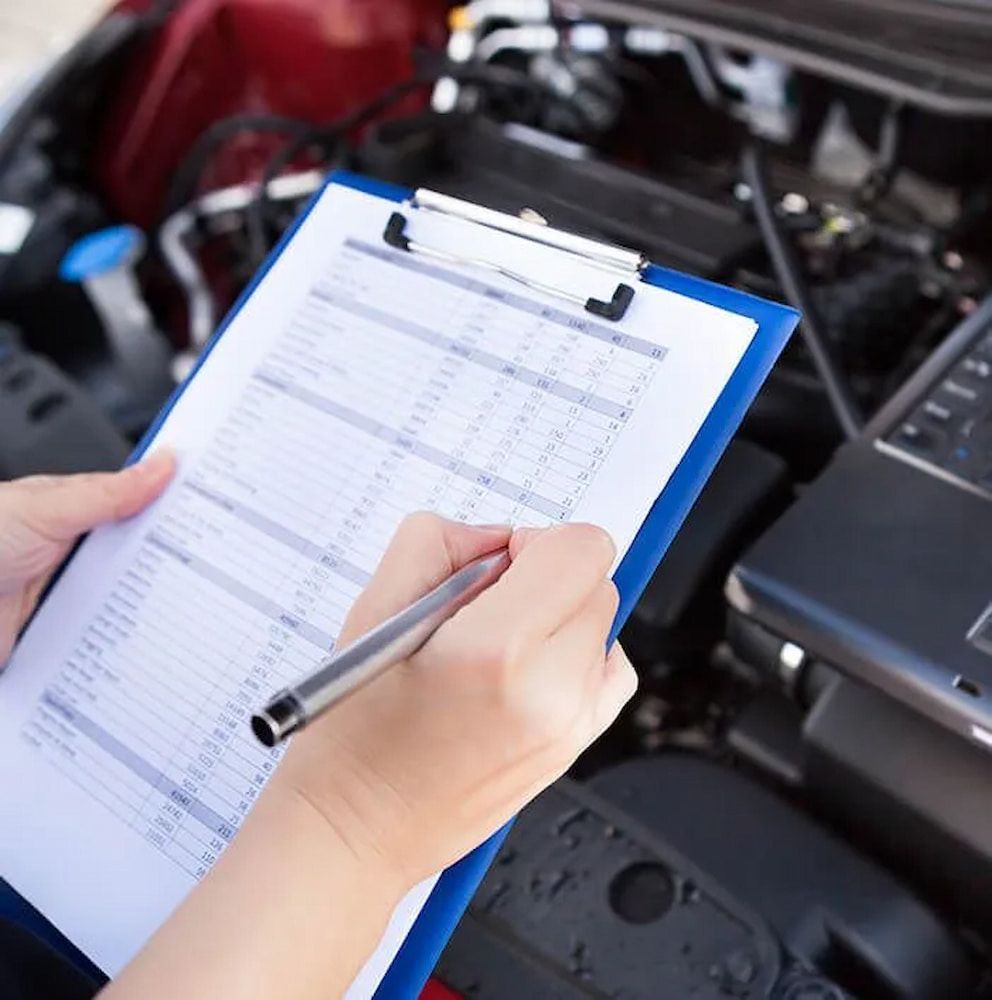 A Person Is Writing On A Clipboard In Front Of A Car Engine — Figtree Brake and Clutch in Figtree, NSW