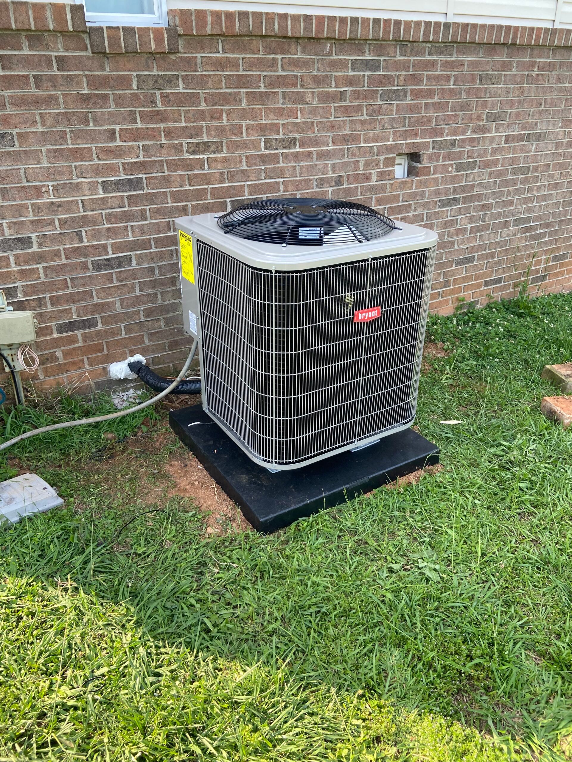 A large air conditioner is sitting in the grass next to a brick wall.