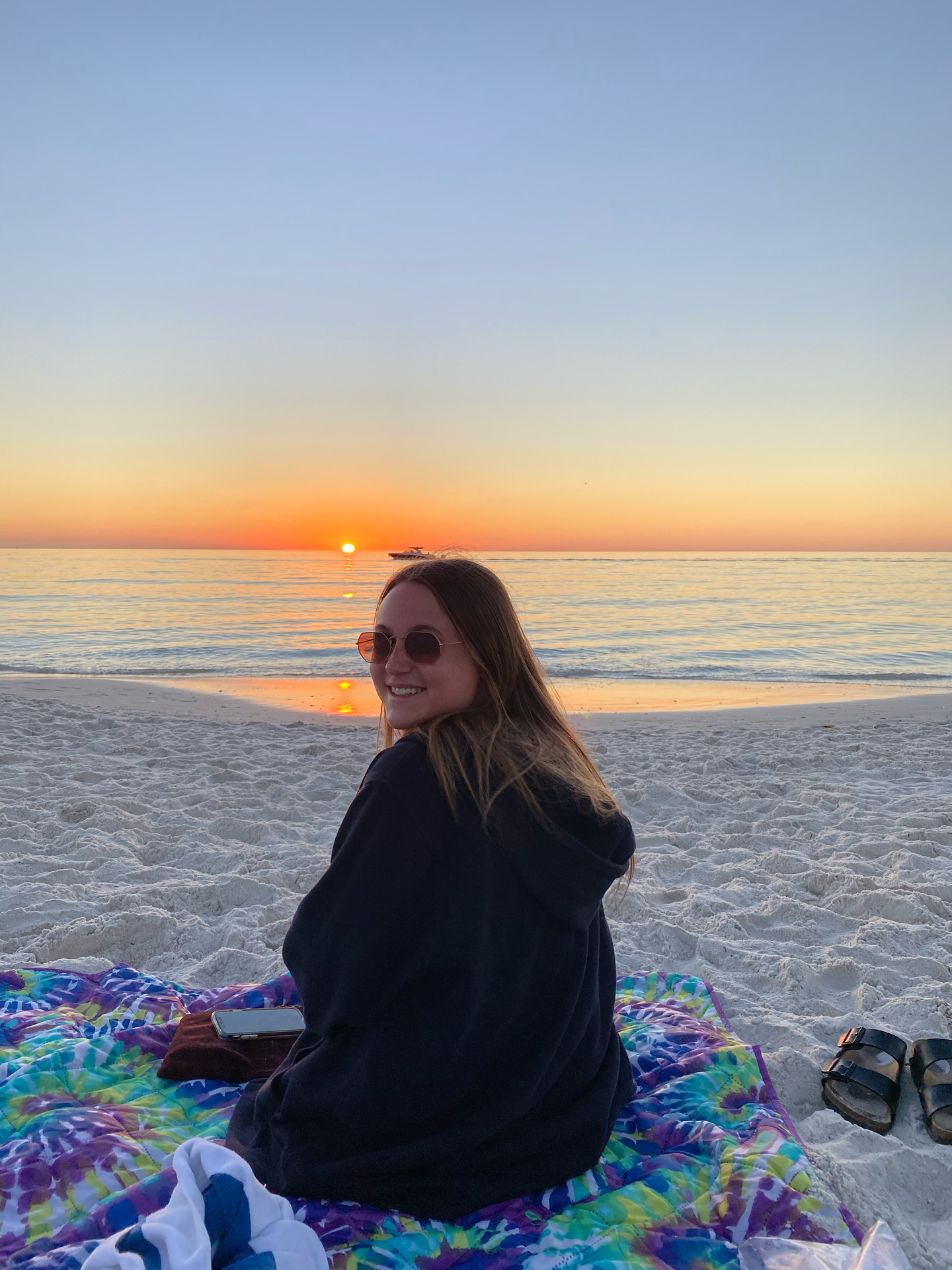 Madison is sitting on a blanket on the beach at sunset in Flordia.