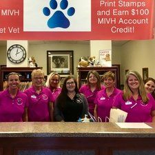 Veterinary clinic staff smiling behind a counter; sign with paw print logo and text about credit.