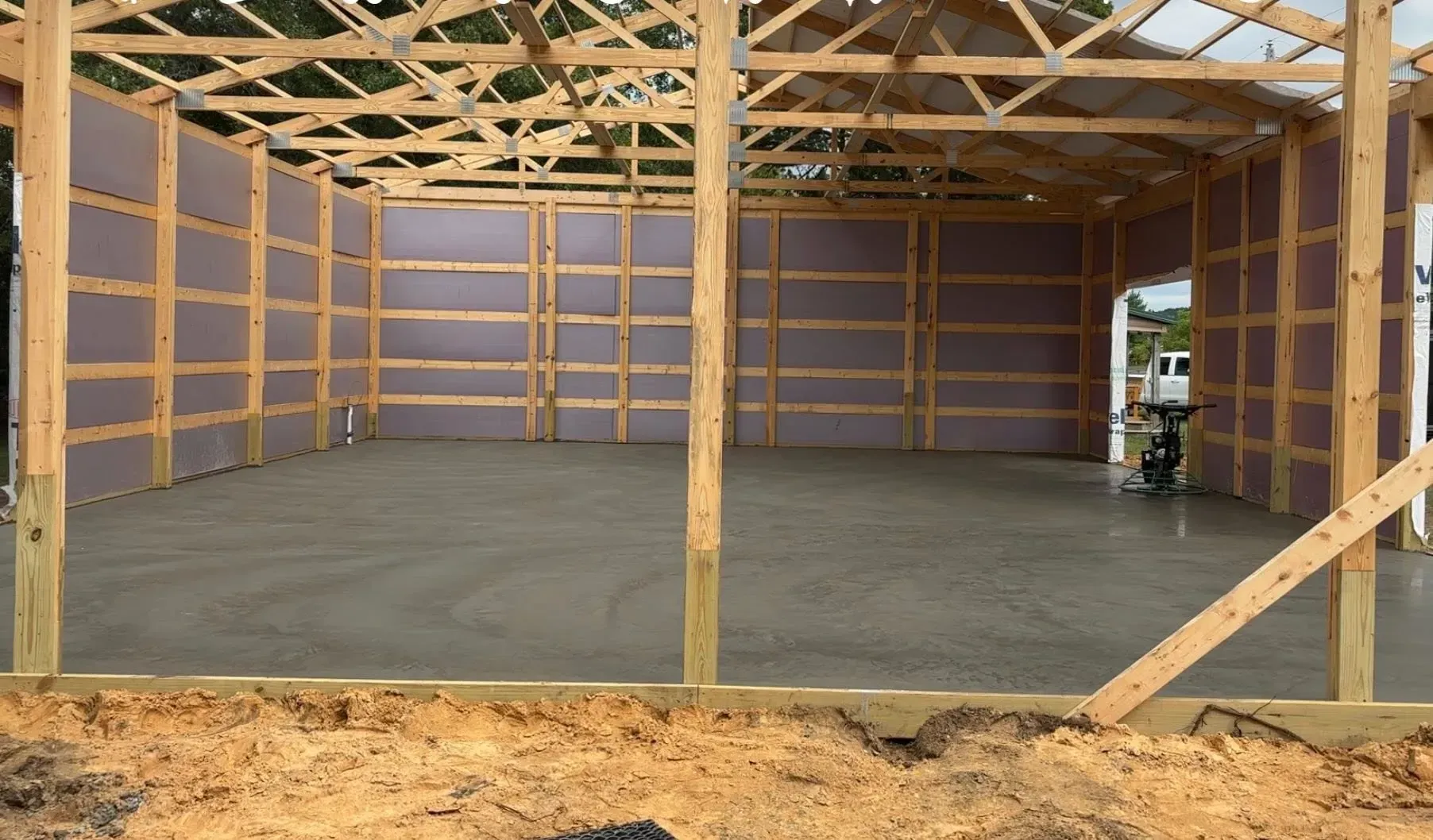 Interior of a wood-framed pole barn structure with insulated walls and a newly poured concrete floor.