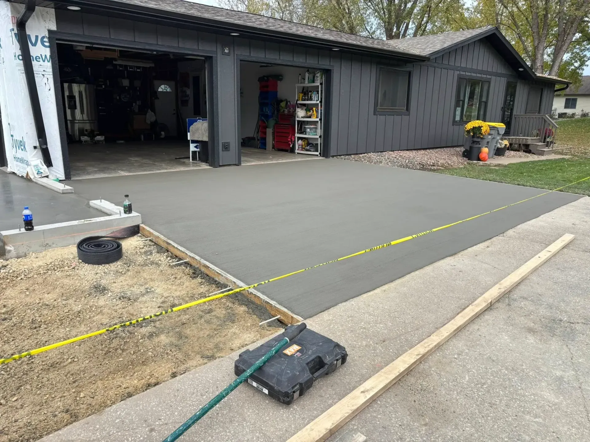 Freshly poured concrete driveway extension in front of a dark gray house with an open garage.