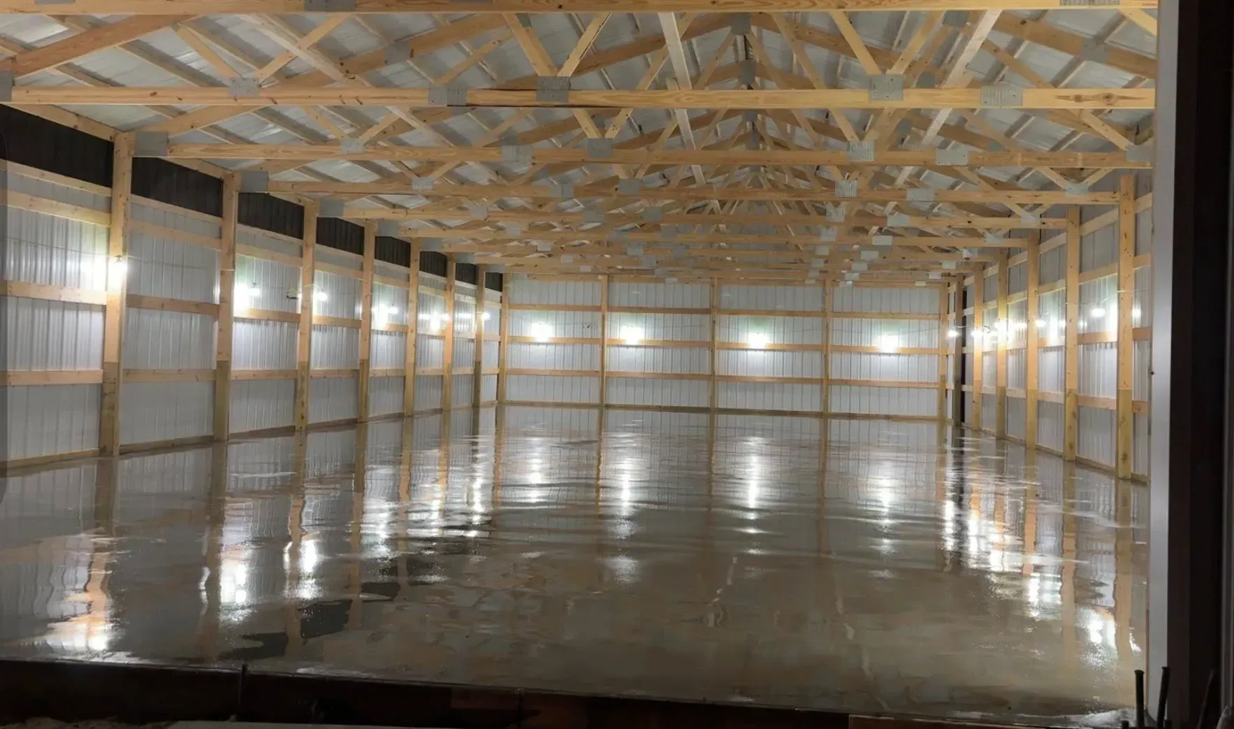 A spacious, empty pole barn with a polished concrete floor, exposed wooden trusses, and white metal-lined walls.