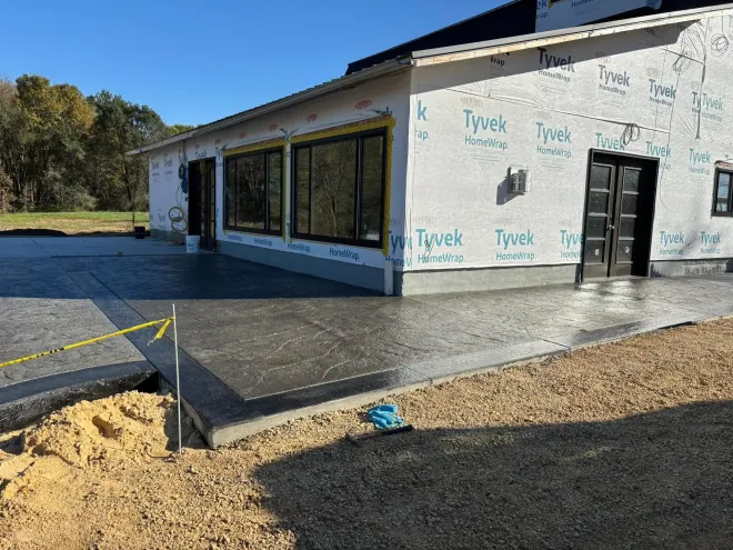 A side view of a house under construction with a patterned stamped concrete patio and Tyvek house wrap on the exterior.