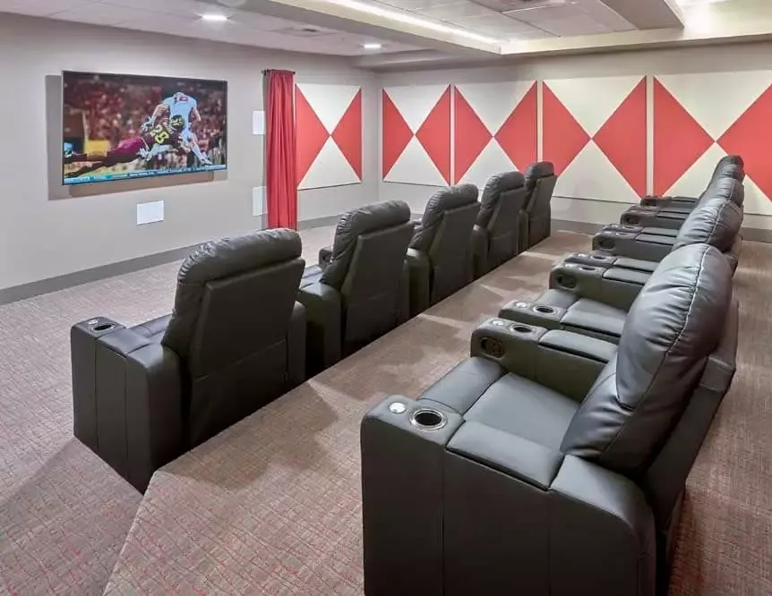 A row of black leather chairs in a theater with a flat screen tv.