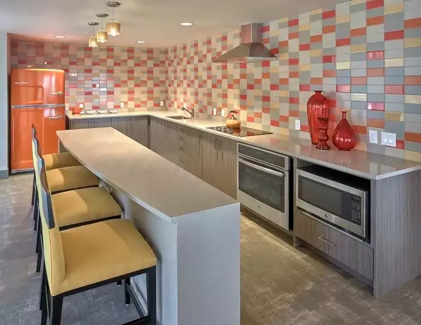 A kitchen with a long counter and chairs and a refrigerator.