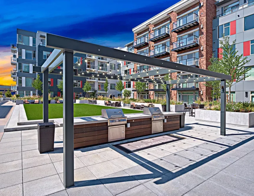 A patio with a grill and a pergola in front of a building.