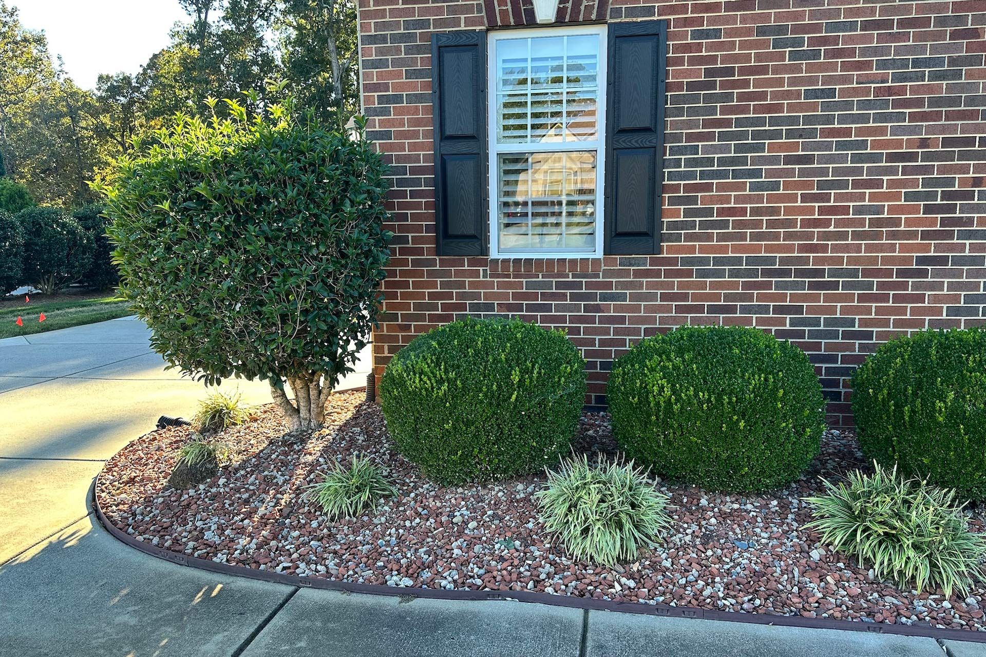 Brick house with black shutters, green bushes, and reddish-brown gravel landscaping.