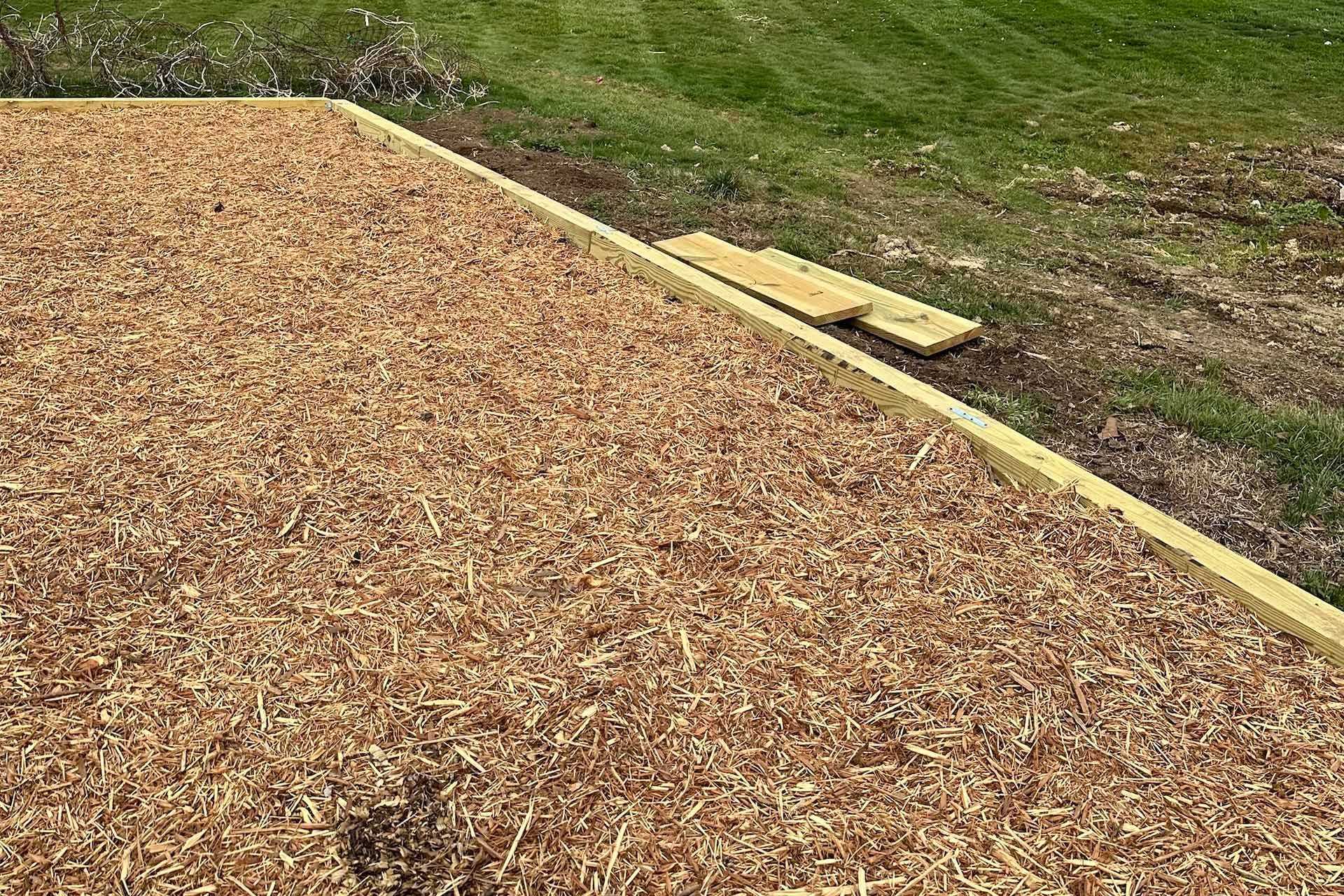 Play area covered in wood chips, edged with wood boards, next to grass.