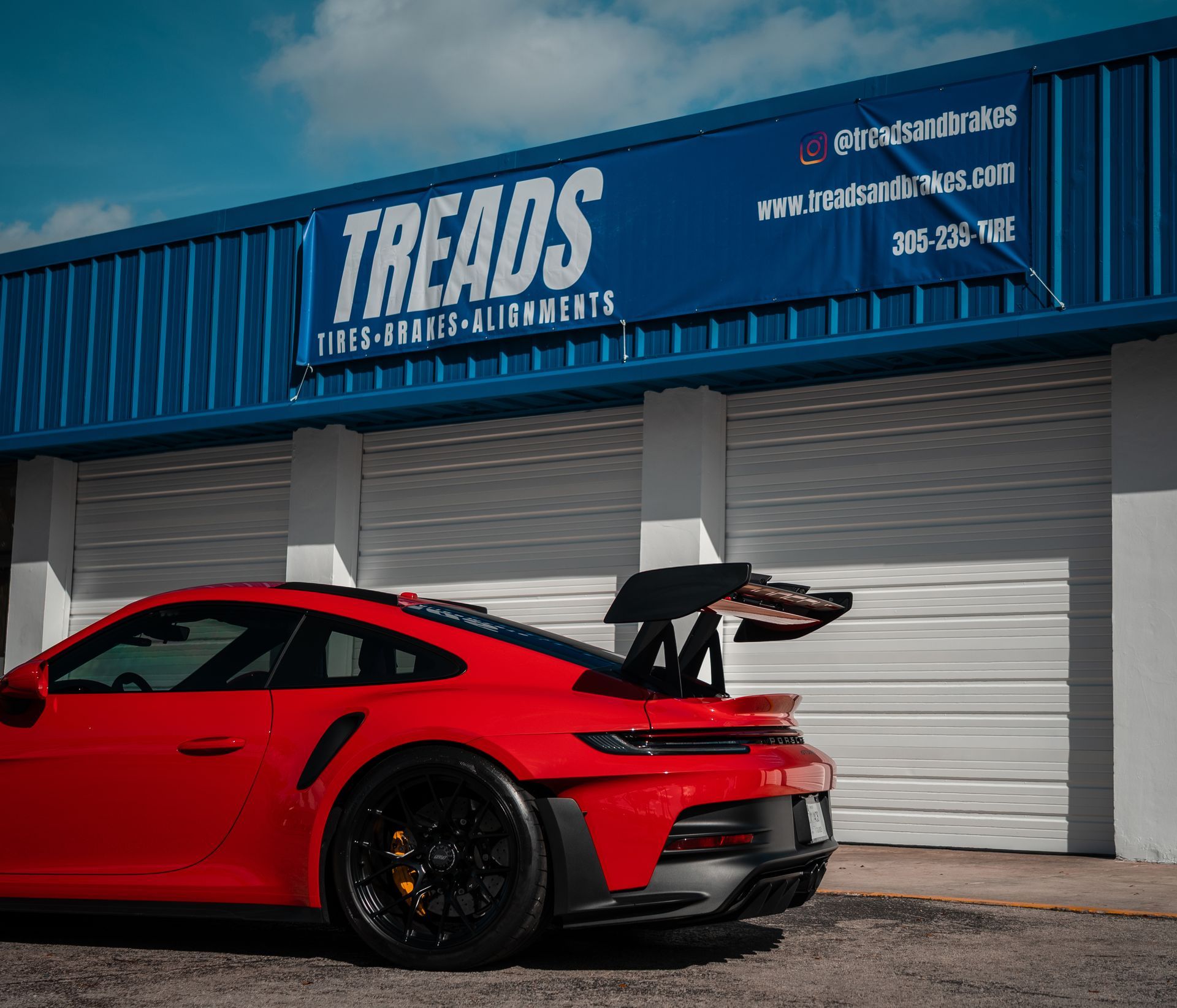 Red sports car with large rear wing parked outside Treads auto shop.