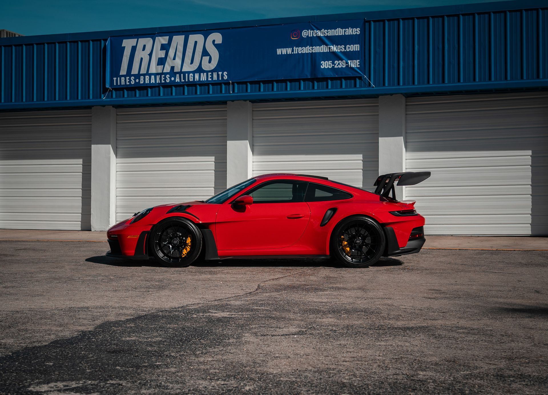 Red sports car with a large rear wing parked in front of a Treads storefront