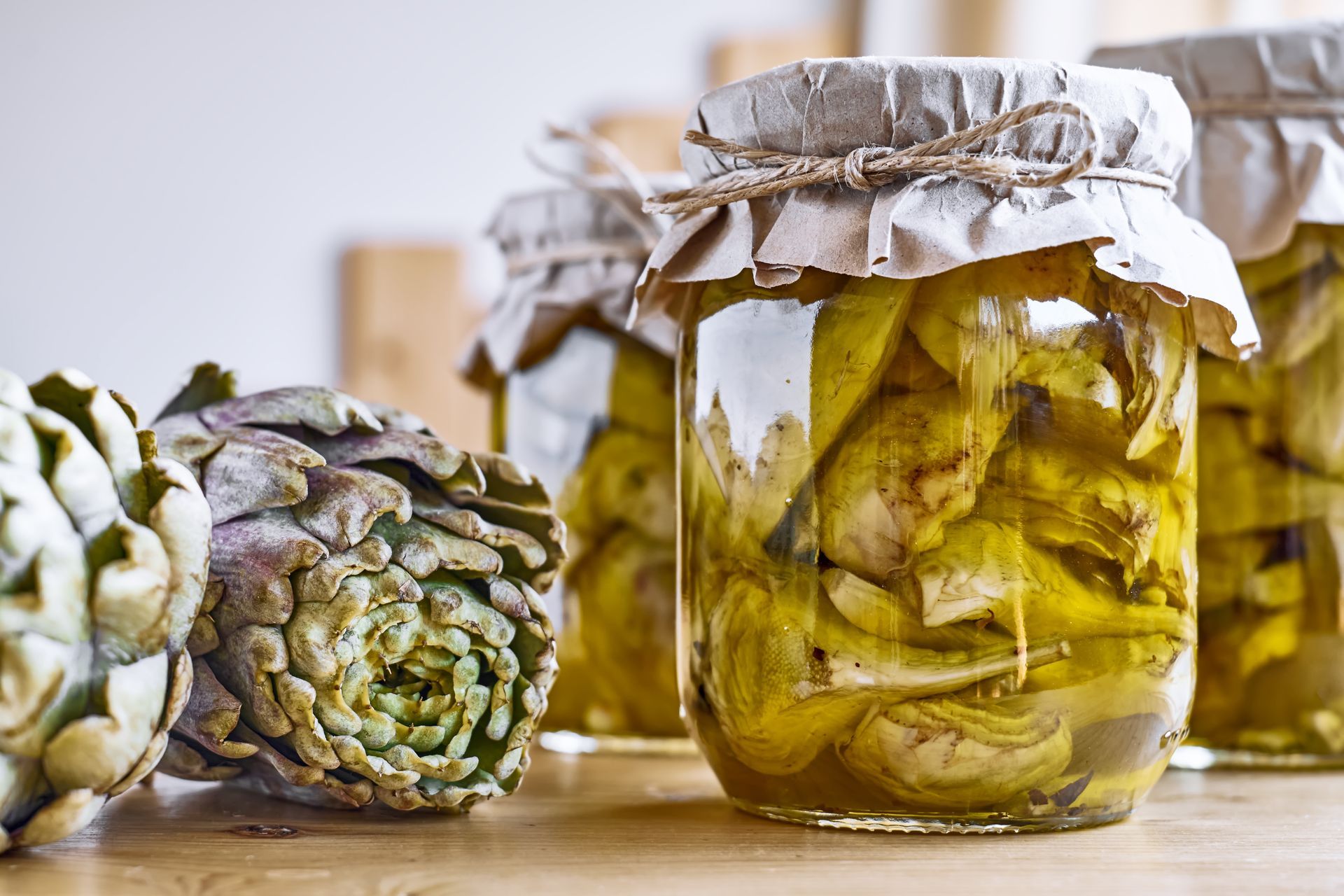 Tre barattoli di carciofi sono appoggiati su un tavolo di legno.