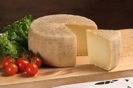 Un pezzo di formaggio è appoggiato su un tagliere di legno accanto a pomodori e lattuga.