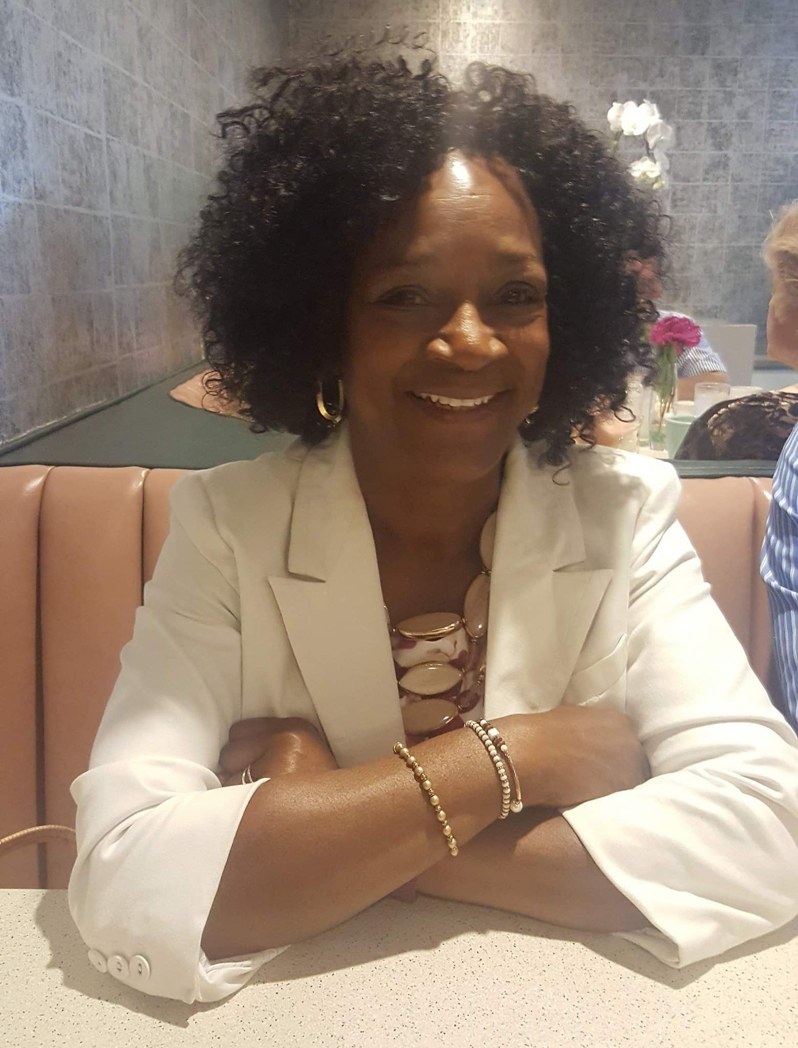 A woman is sitting at a table with her arms crossed and smiling.