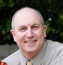 A bald man wearing a shirt and tie is smiling for the camera.