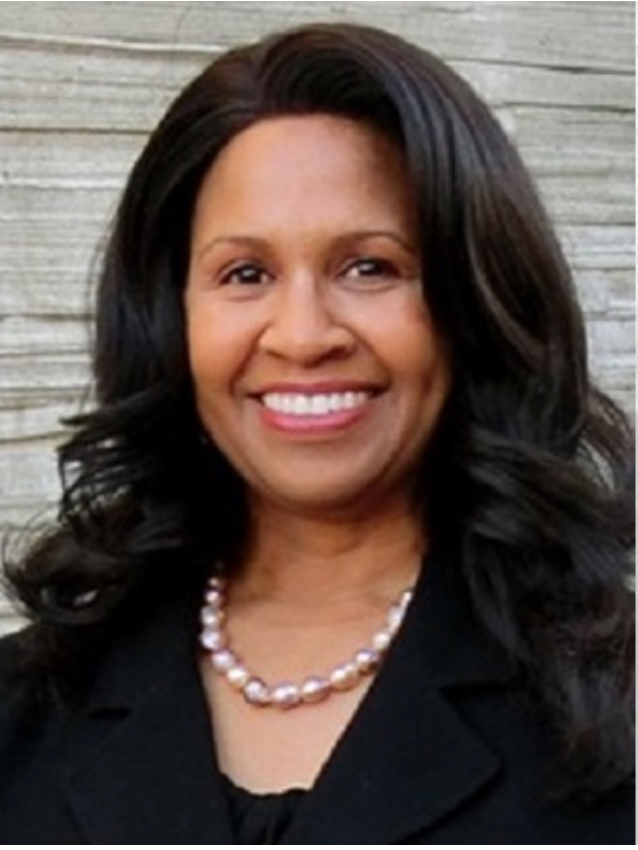A woman wearing a pearl necklace and a black jacket smiles for the camera