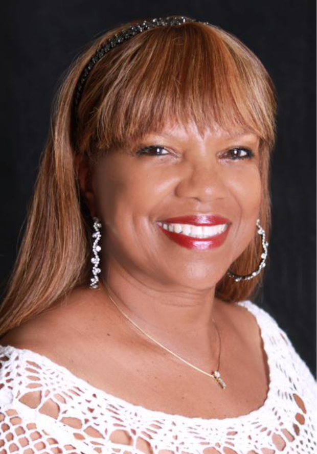 A woman wearing a white top and earrings is smiling for the camera.
