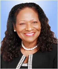 A woman with curly hair and a pearl necklace is smiling for the camera.