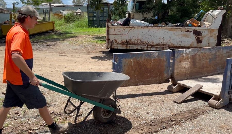 A Man is Pushing a Wheelbarrow in a Dirt Field — Bin Hire in Maryborough, QLD