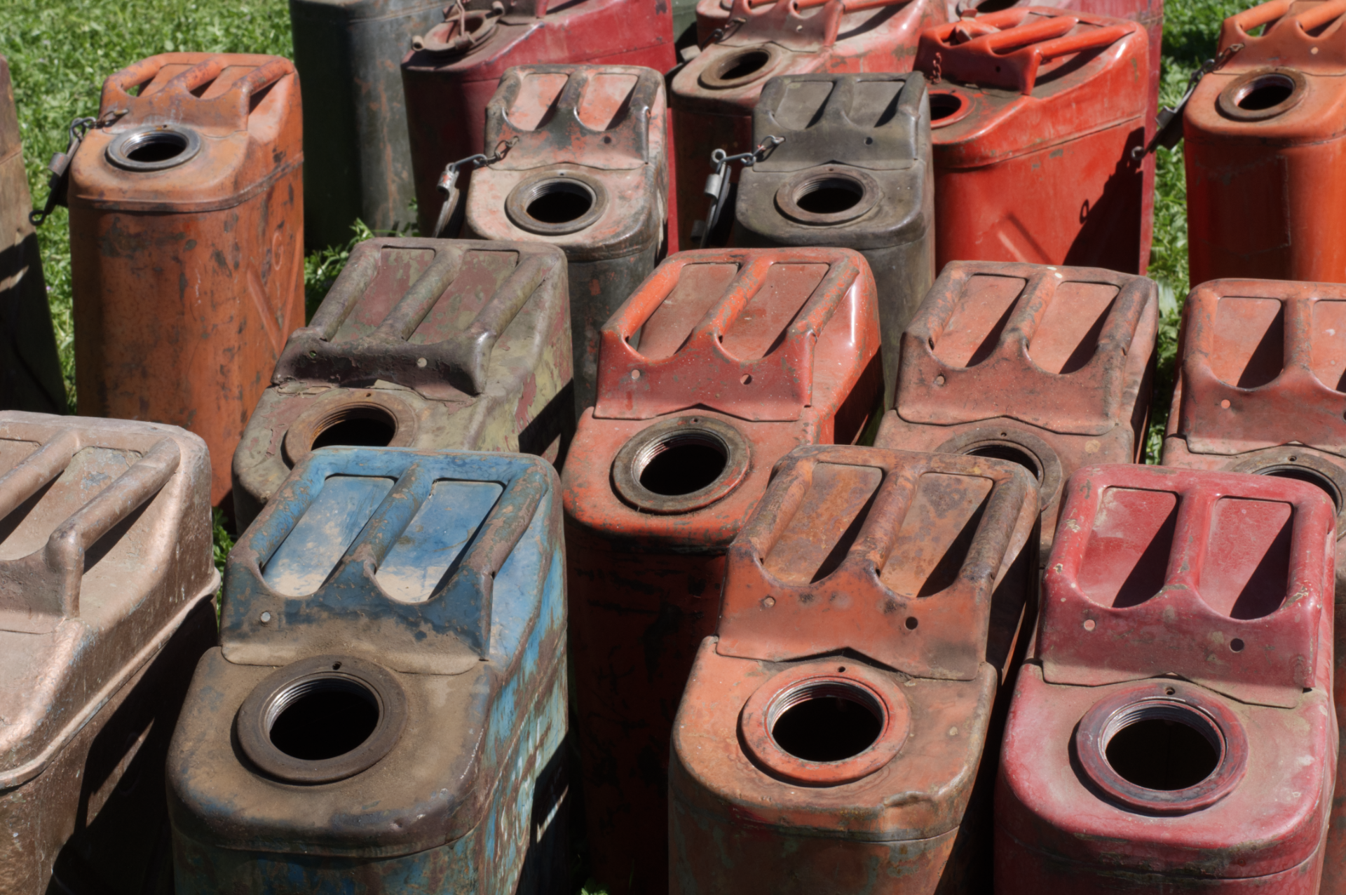 Stacked old metal jerry cans in rusted red, gray, and blue colors