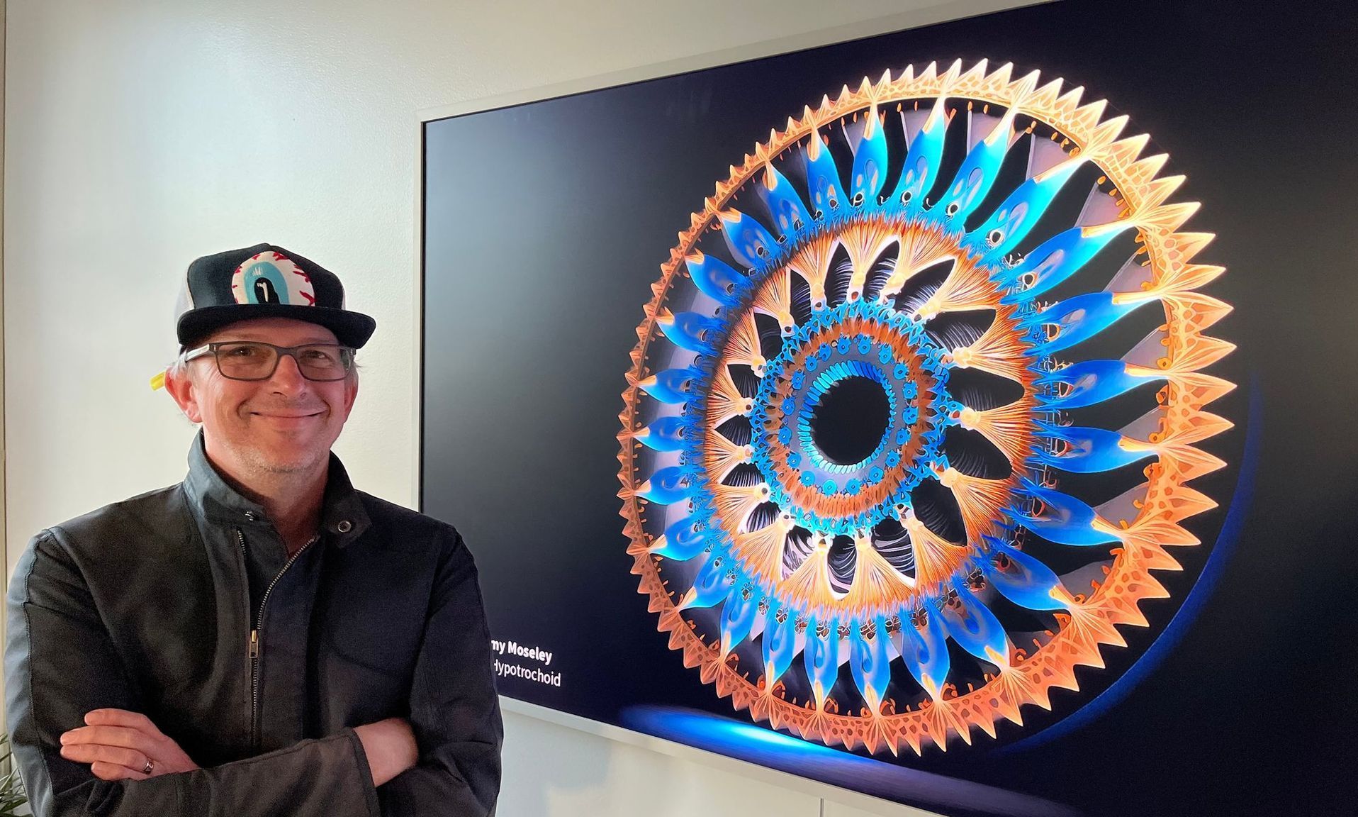 Man standing beside a large colorful circular digital artwork on a wall display