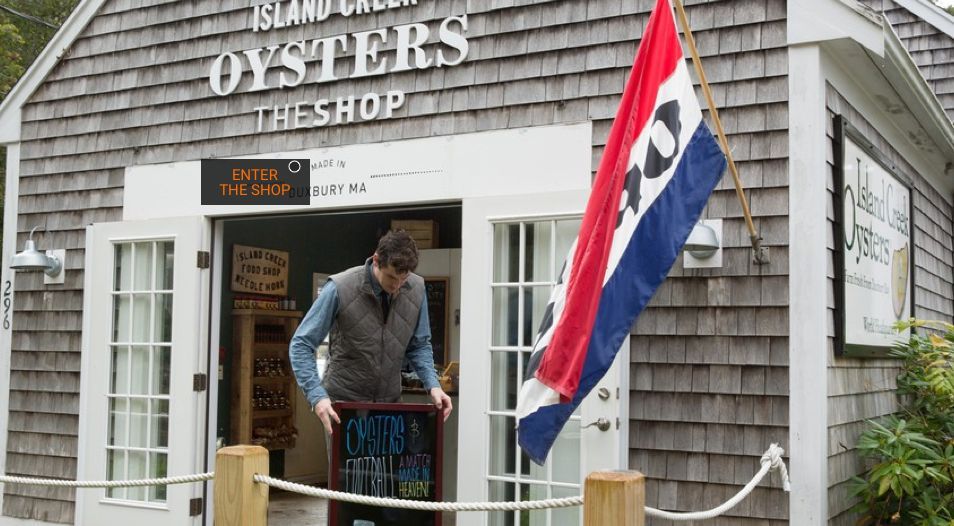 Person carrying a crate outside a seafood shop with a hanging Maine flag.