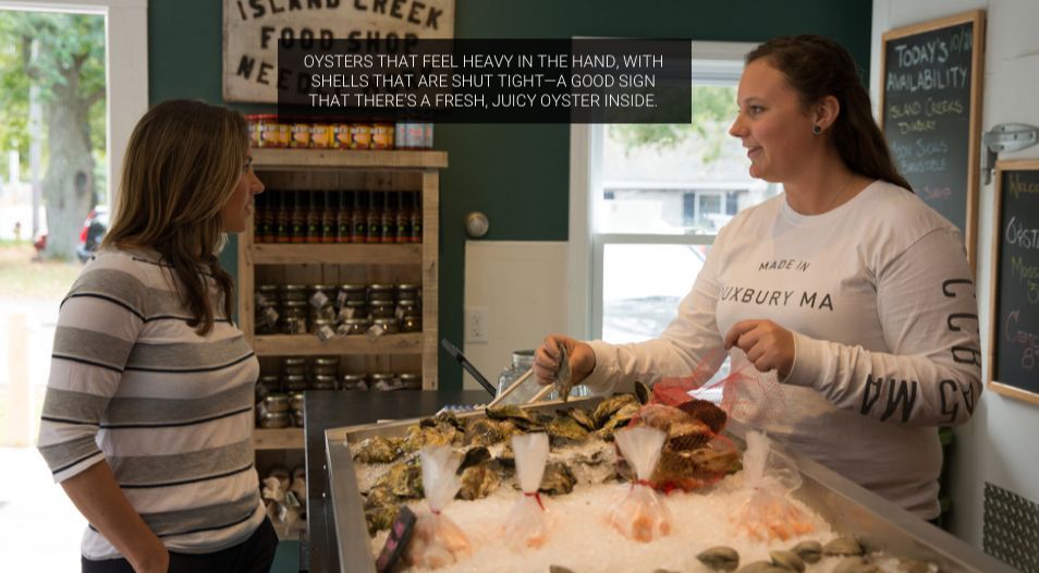 Two women chatting at a seafood counter in a market, with ice display and menu board behind them