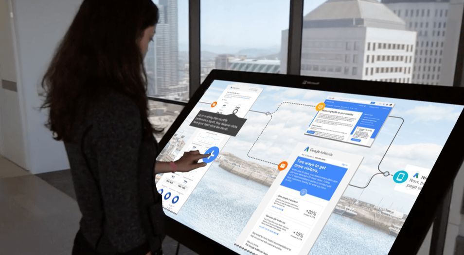 Person using a large touchscreen display in a bright office overlooking a city skyline