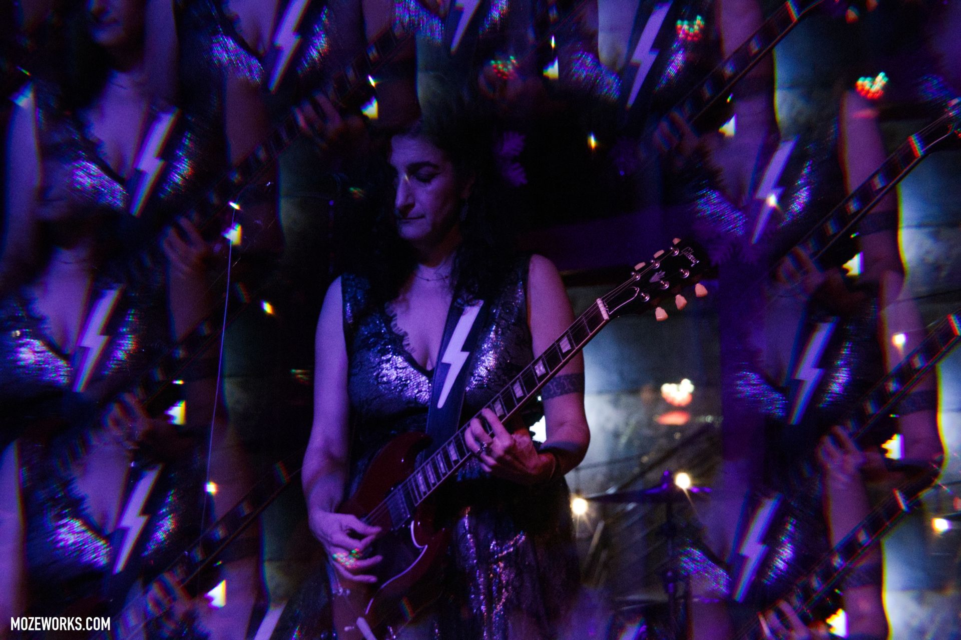 Woman playing guitar on a dimly lit stage with purple lighting and hanging decorations