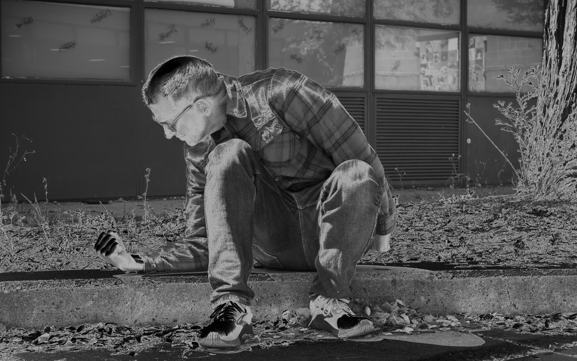 Person crouching on pavement outdoors, reaching toward the ground in front of a building.