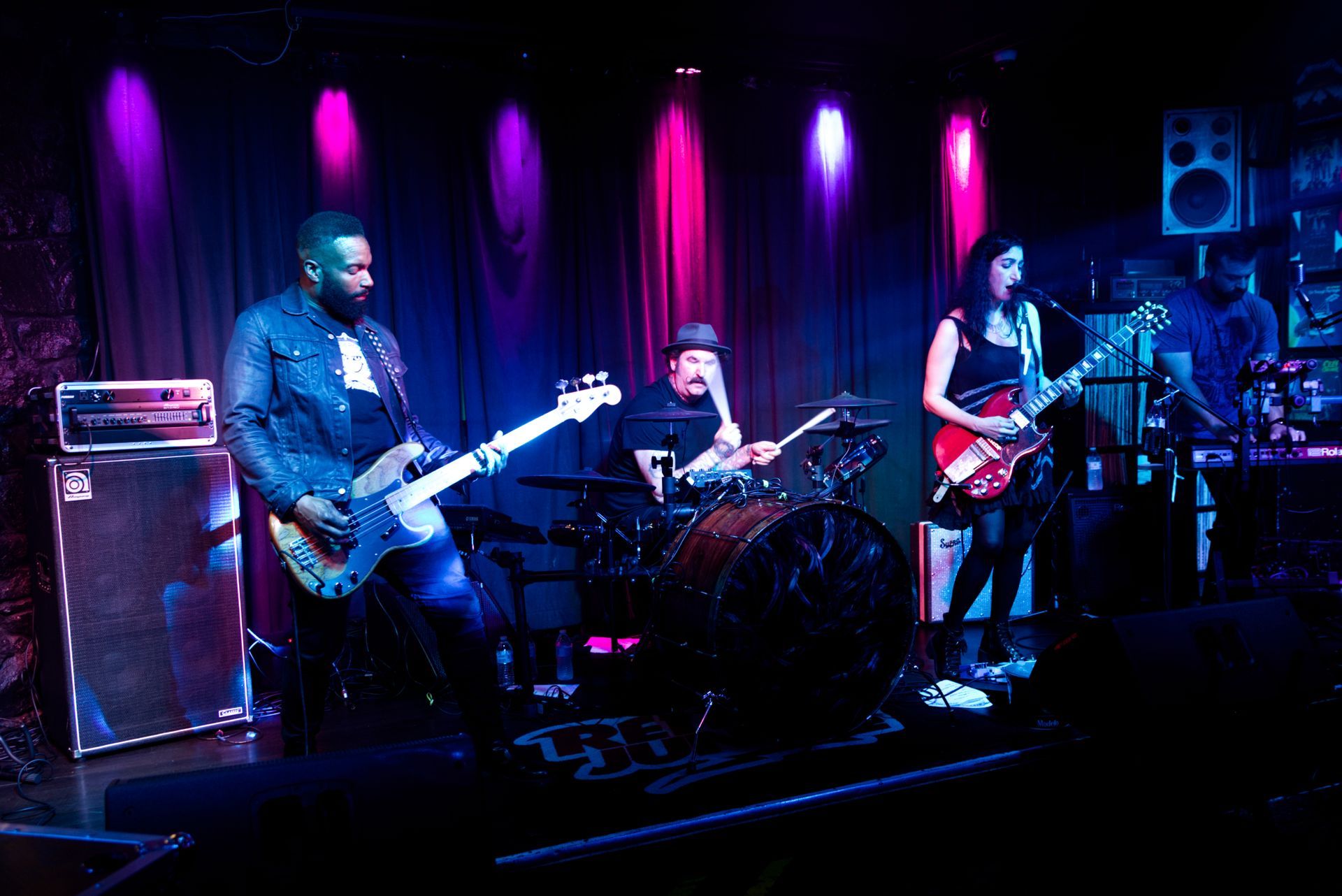 Live band performing on a dim purple-lit stage with guitars and drums