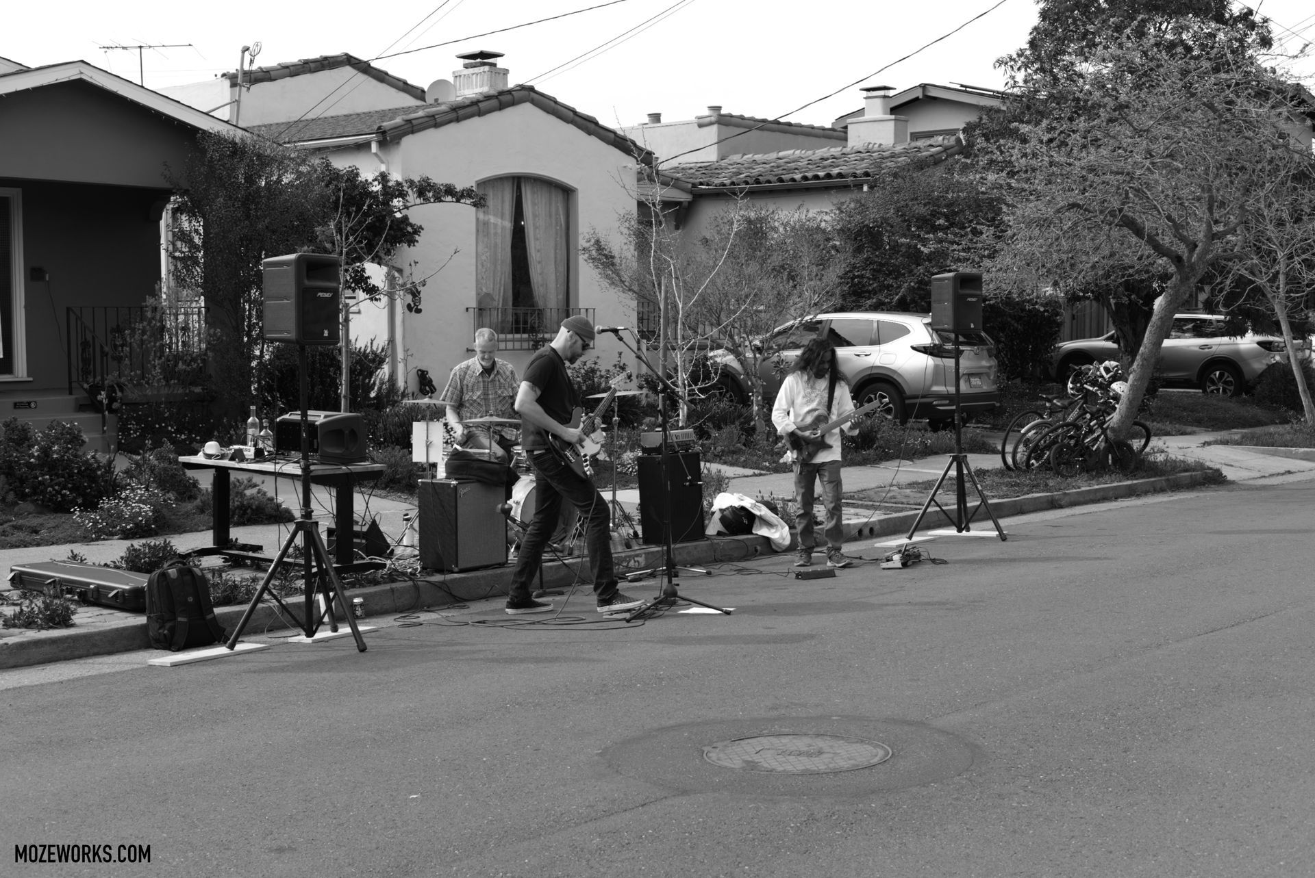 Film crew setting up cameras on a residential street with houses and parked cars in the background