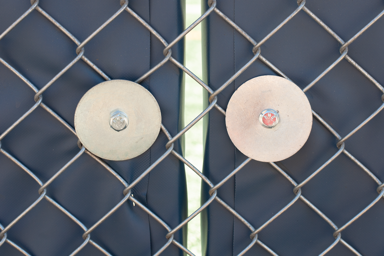 Two round metal fixtures on a chain-link fence, one silver and one white.