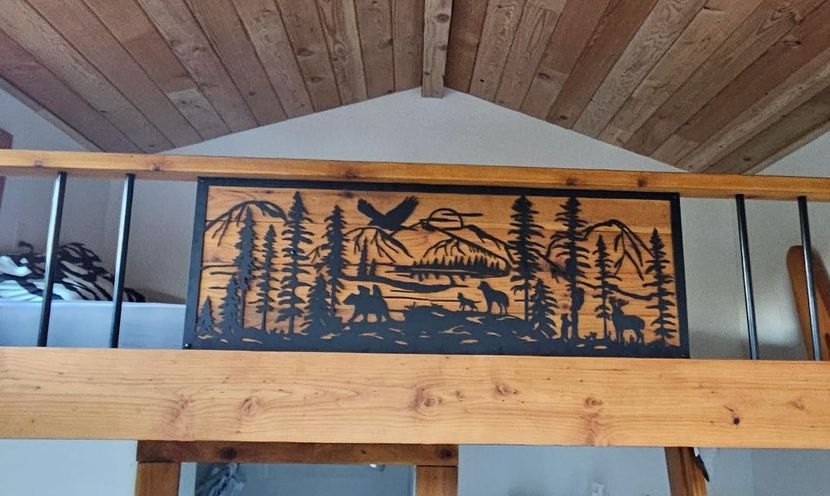 Wooden mountain-and-pine wall art hanging beneath a vaulted wooden ceiling