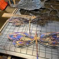 Colorful butterfly-shaped metal wire art pieces arranged on a worktable in a workshop