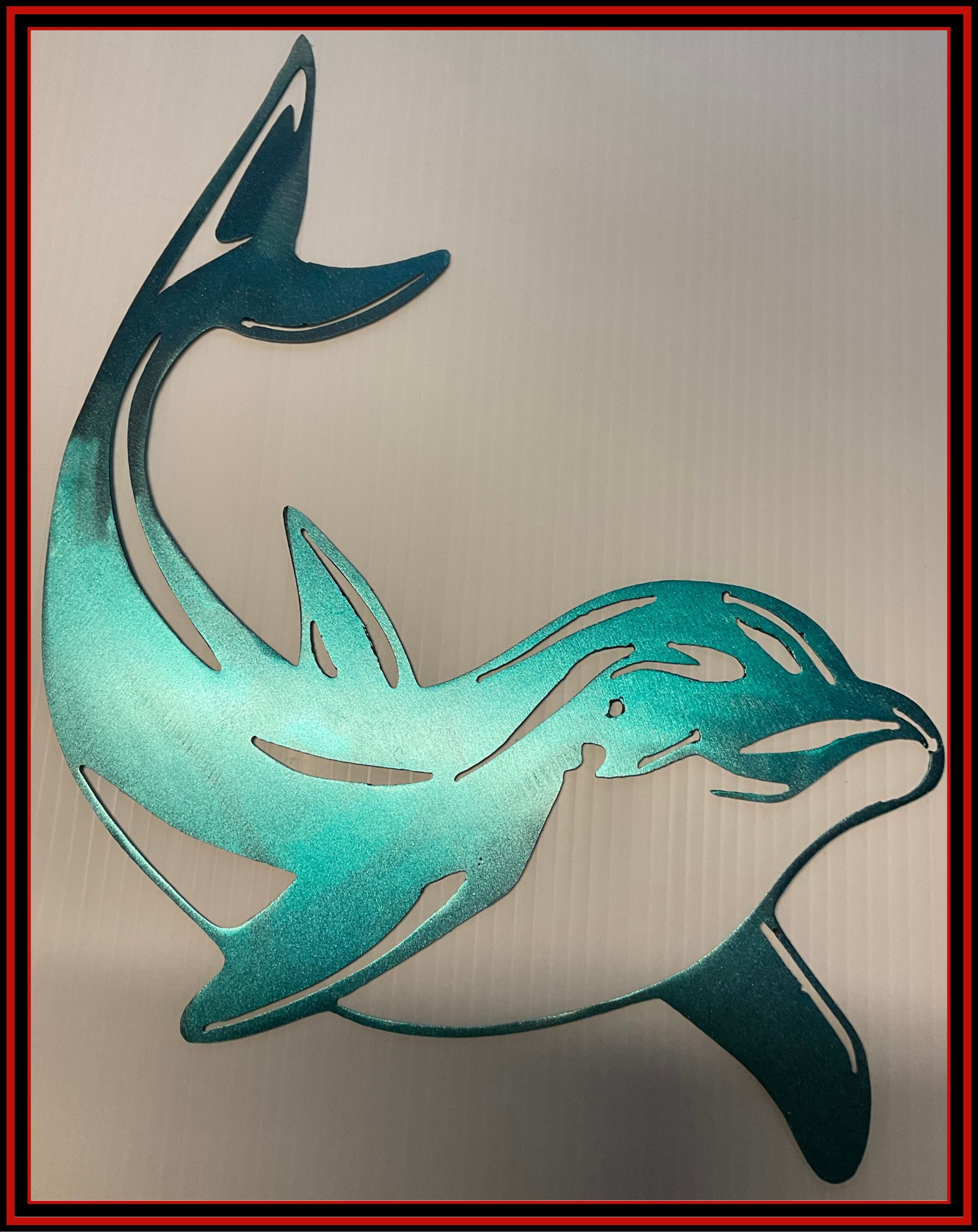 Stylized turquoise dolphin or fish metal wall art on a light background with a red border