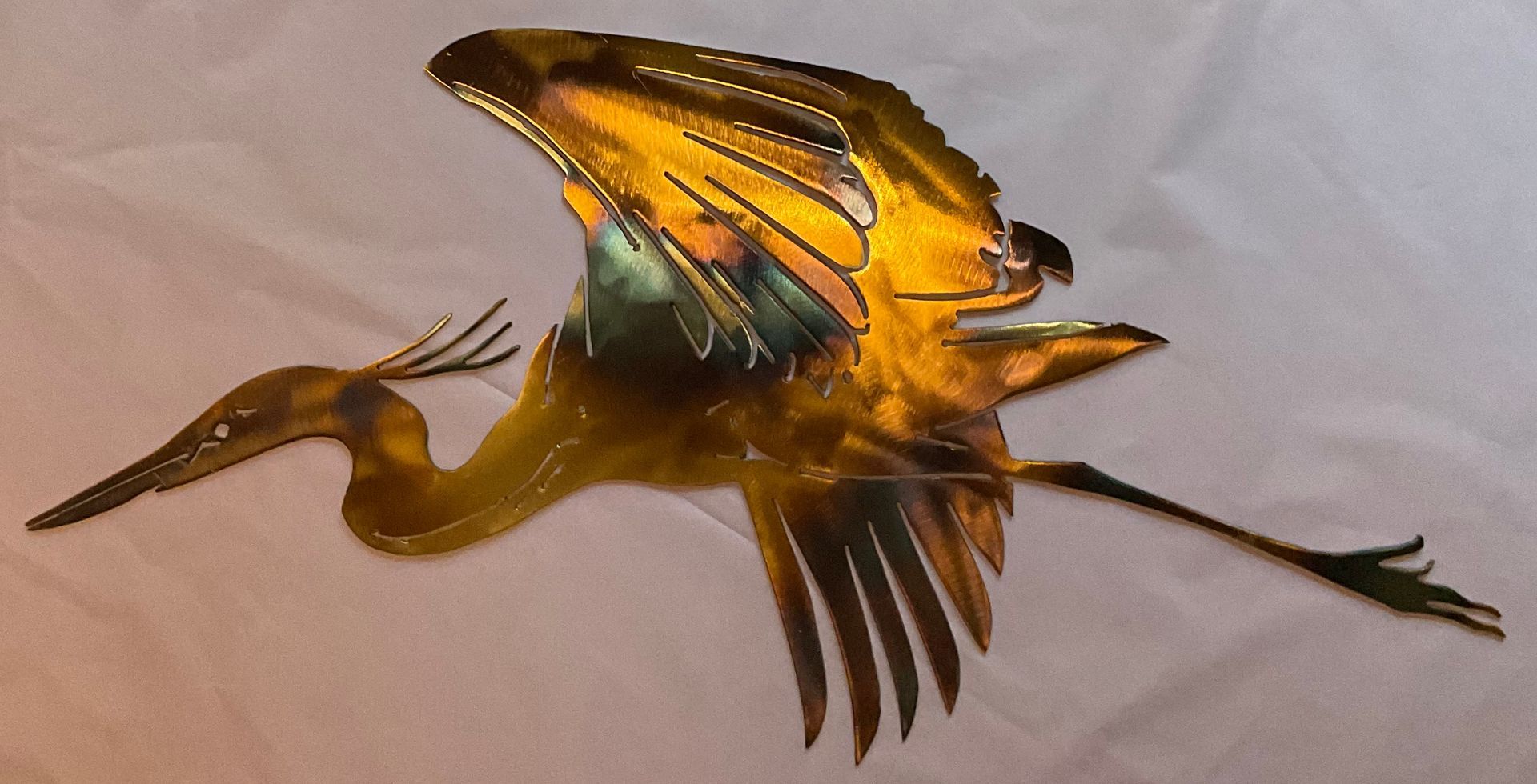 Golden bird sculpture with outstretched wings and long beak, mounted against a white background