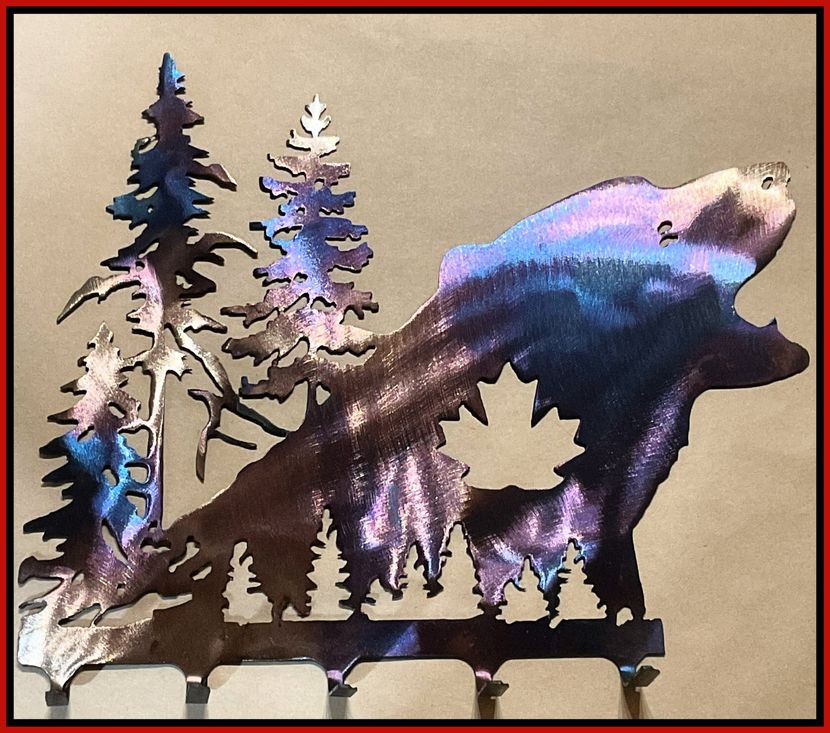 Colorful bear silhouette and pine trees in a rustic metal wall art piece on a tan background
