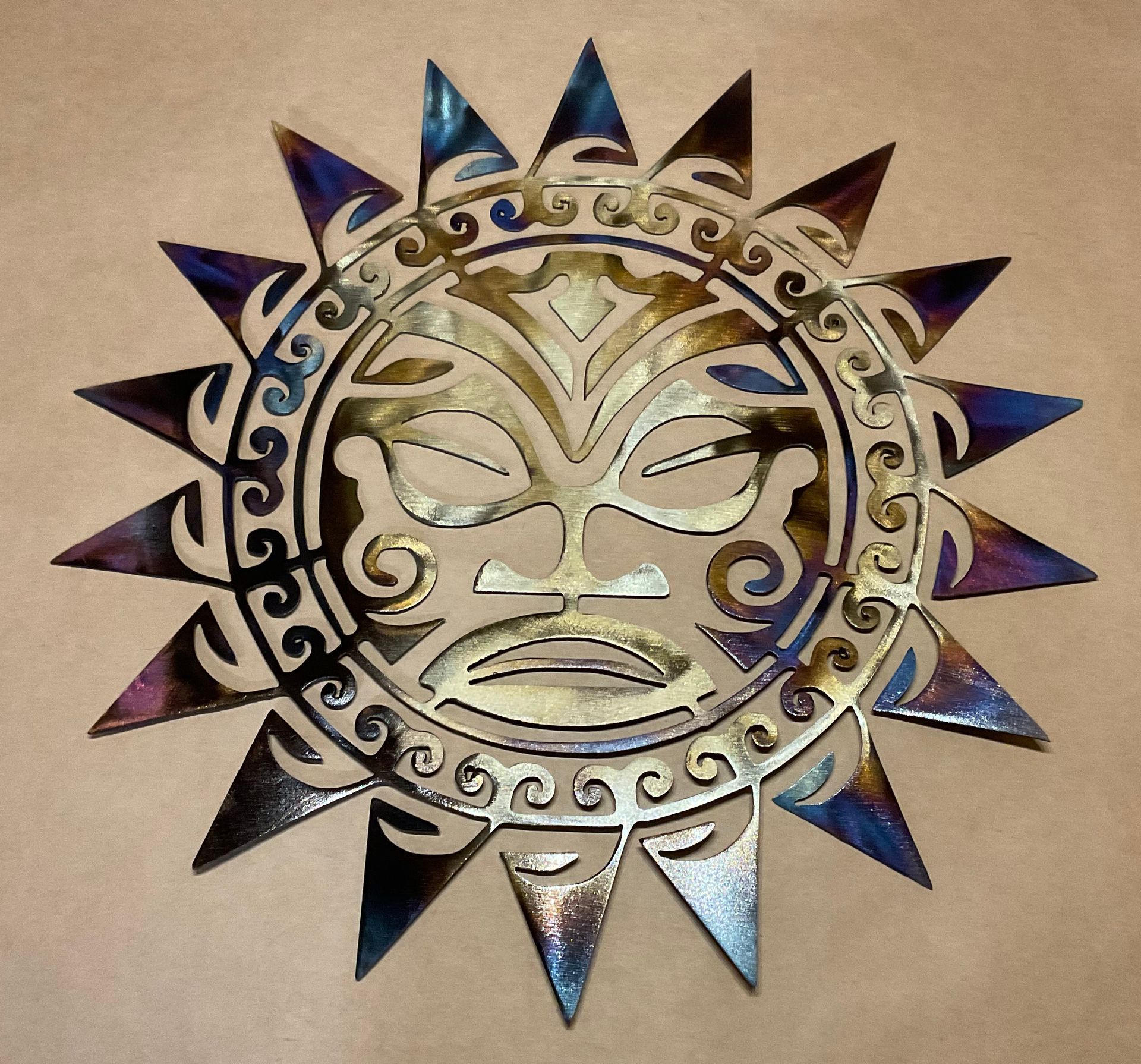 Metal sun face wall decoration with blue and gold accents on a beige background