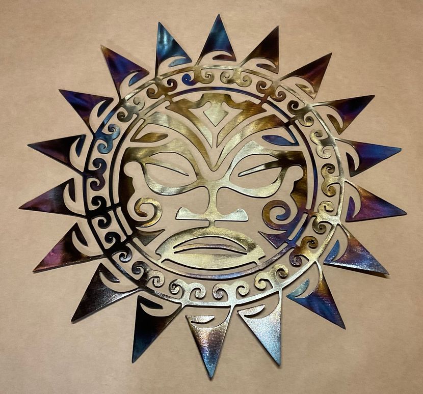 Metal sun face wall art with blue and silver accents on a tan background