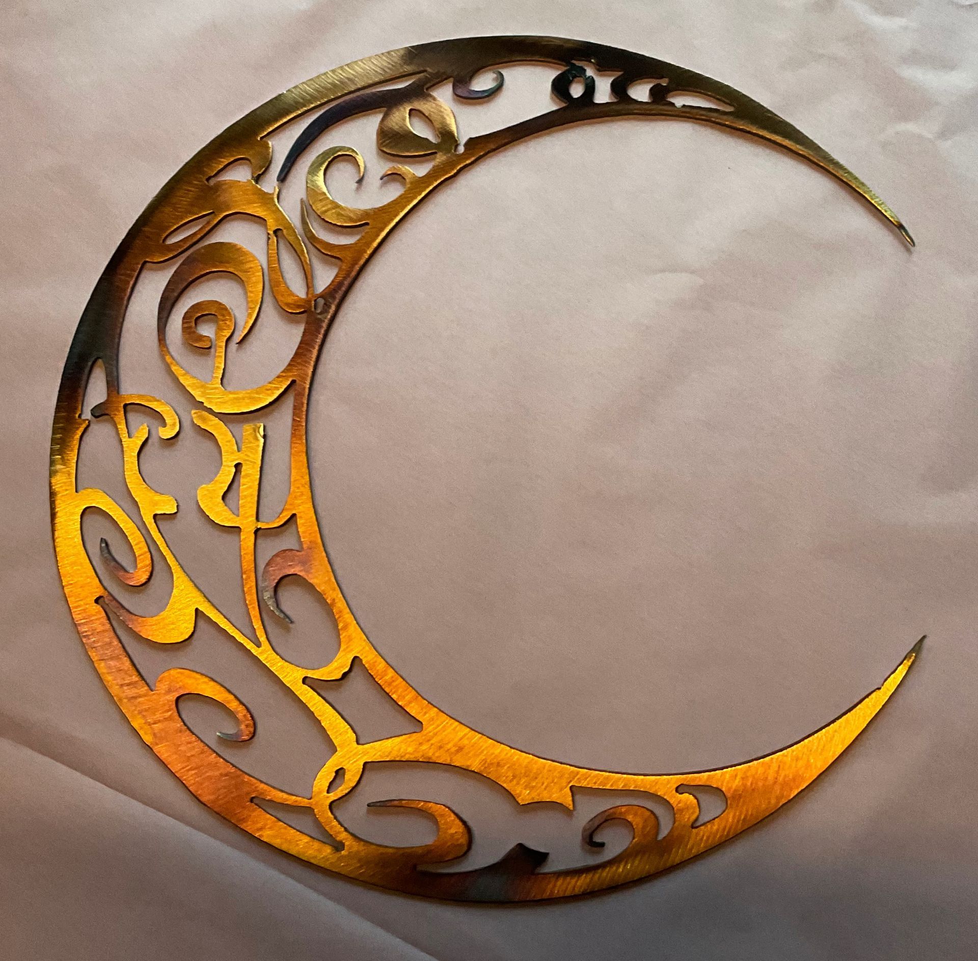 Ornate gold crescent moon cutout with swirling decorative filigree on a beige background