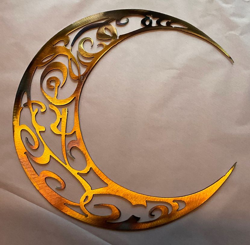 Gold crescent moon ornament with ornate cutout swirls on a light background