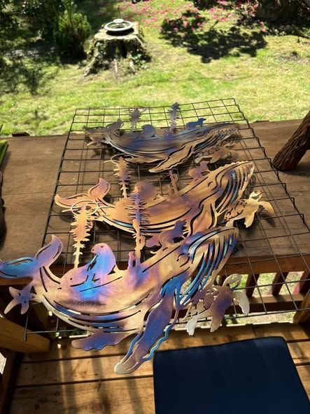 Metal fish sculpture on a wooden table outdoors, with a green yard in the background