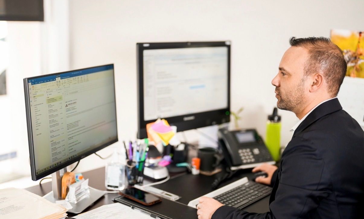 Man in suit working at desk with two computer monitors.