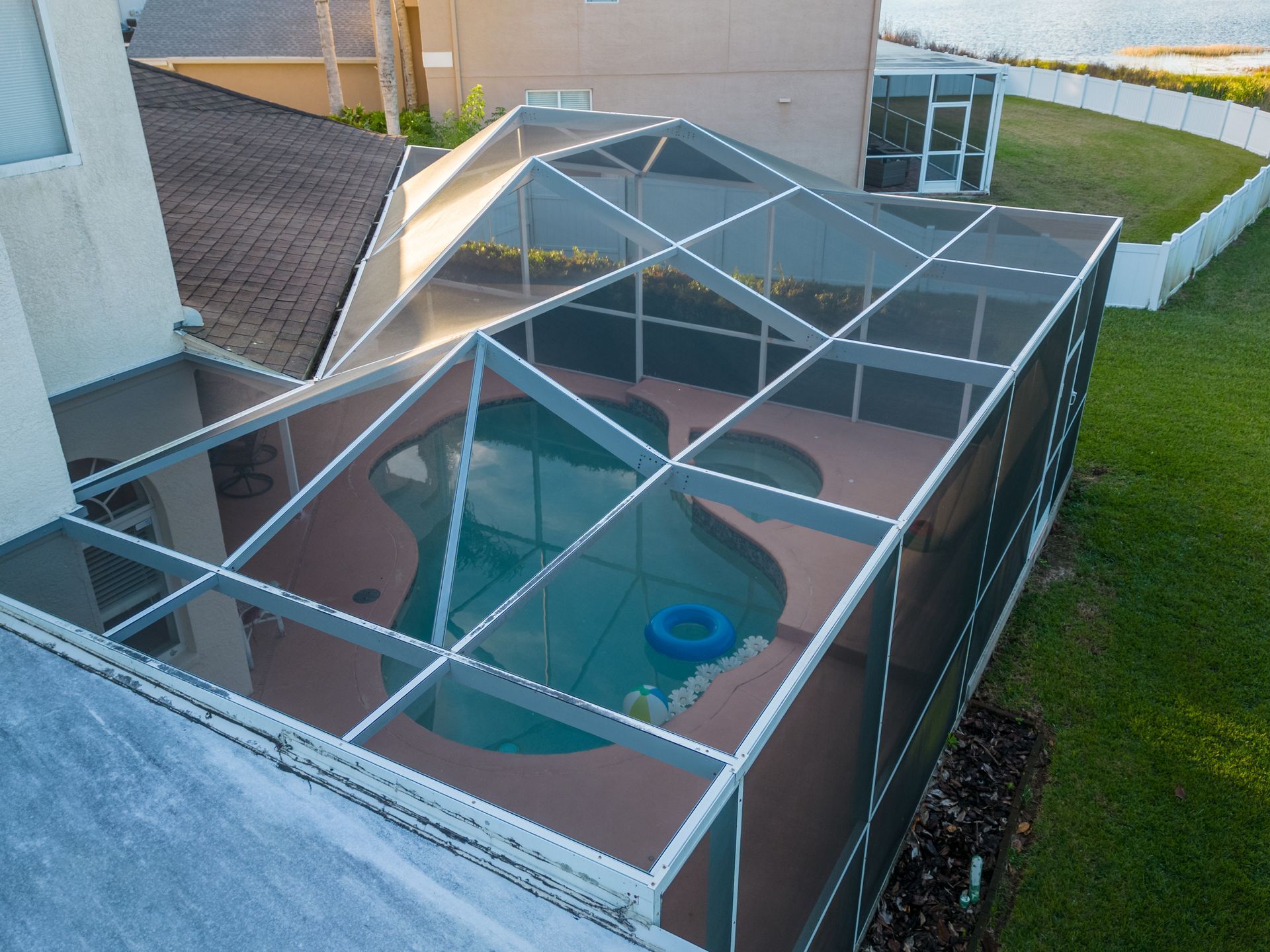 Aerial view of a residential swimming pool protected by a white aluminum patio enclosure. Aerial view of a residential swimming pool protected by a white aluminum patio enclosure.