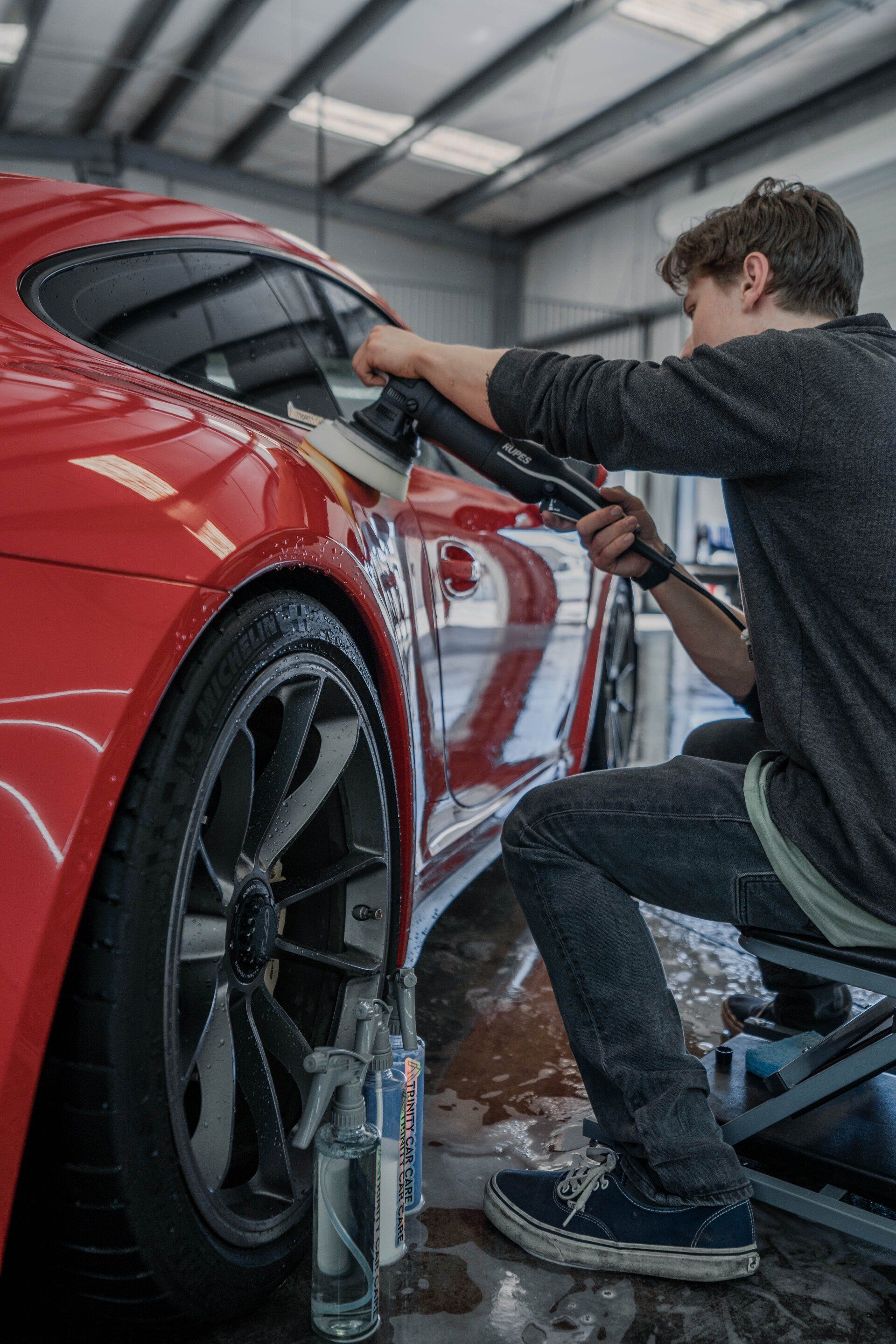 Person polishing a red car with a machine in a garage.