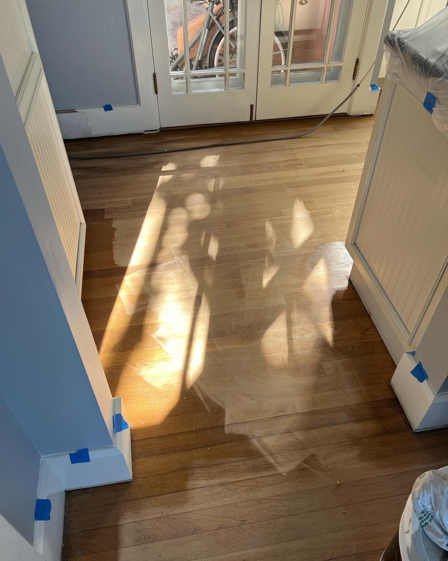 A shadow of a chair is cast on a wooden floor in a kitchen.