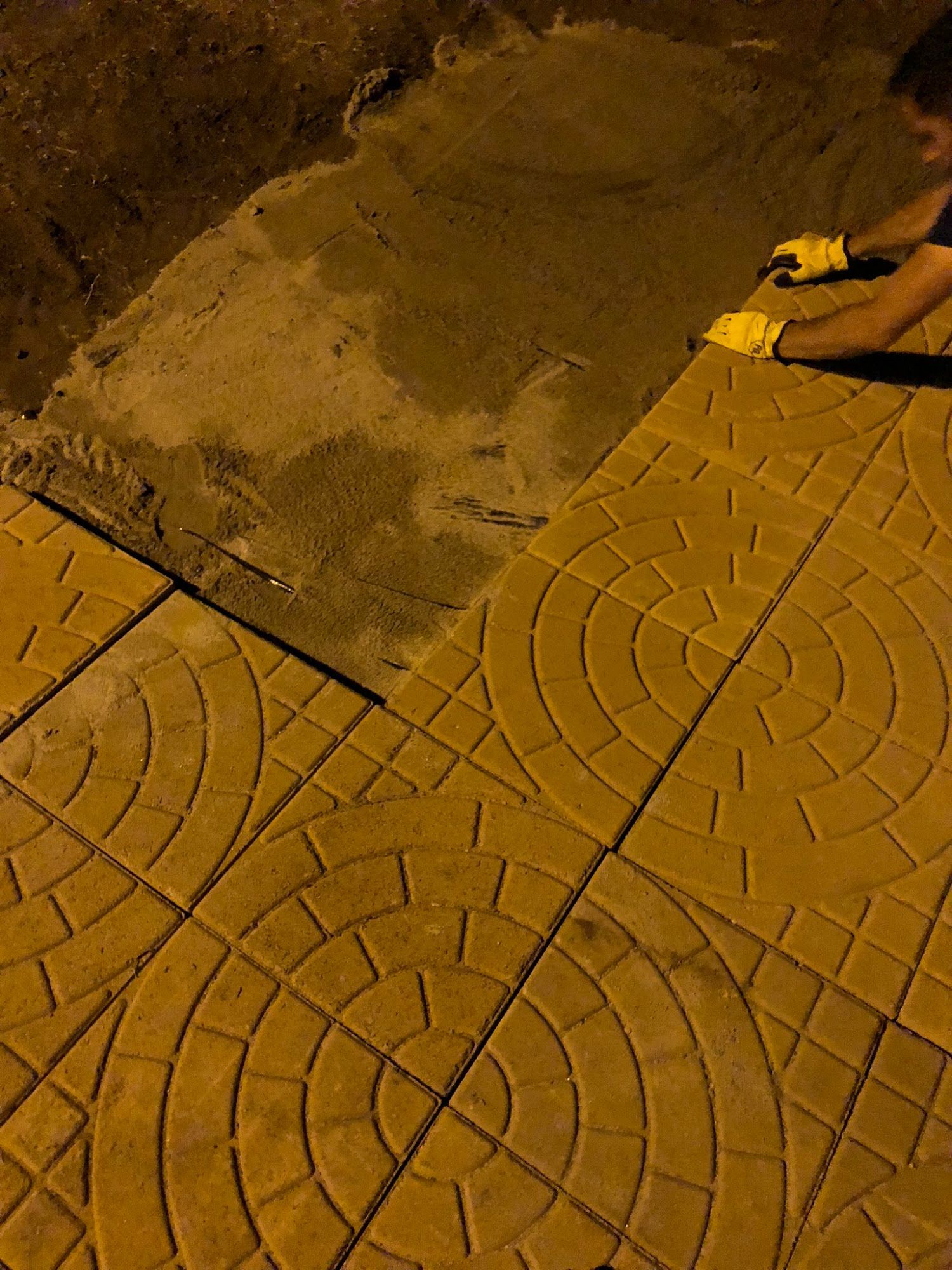 A person wearing yellow gloves is working on a sidewalk