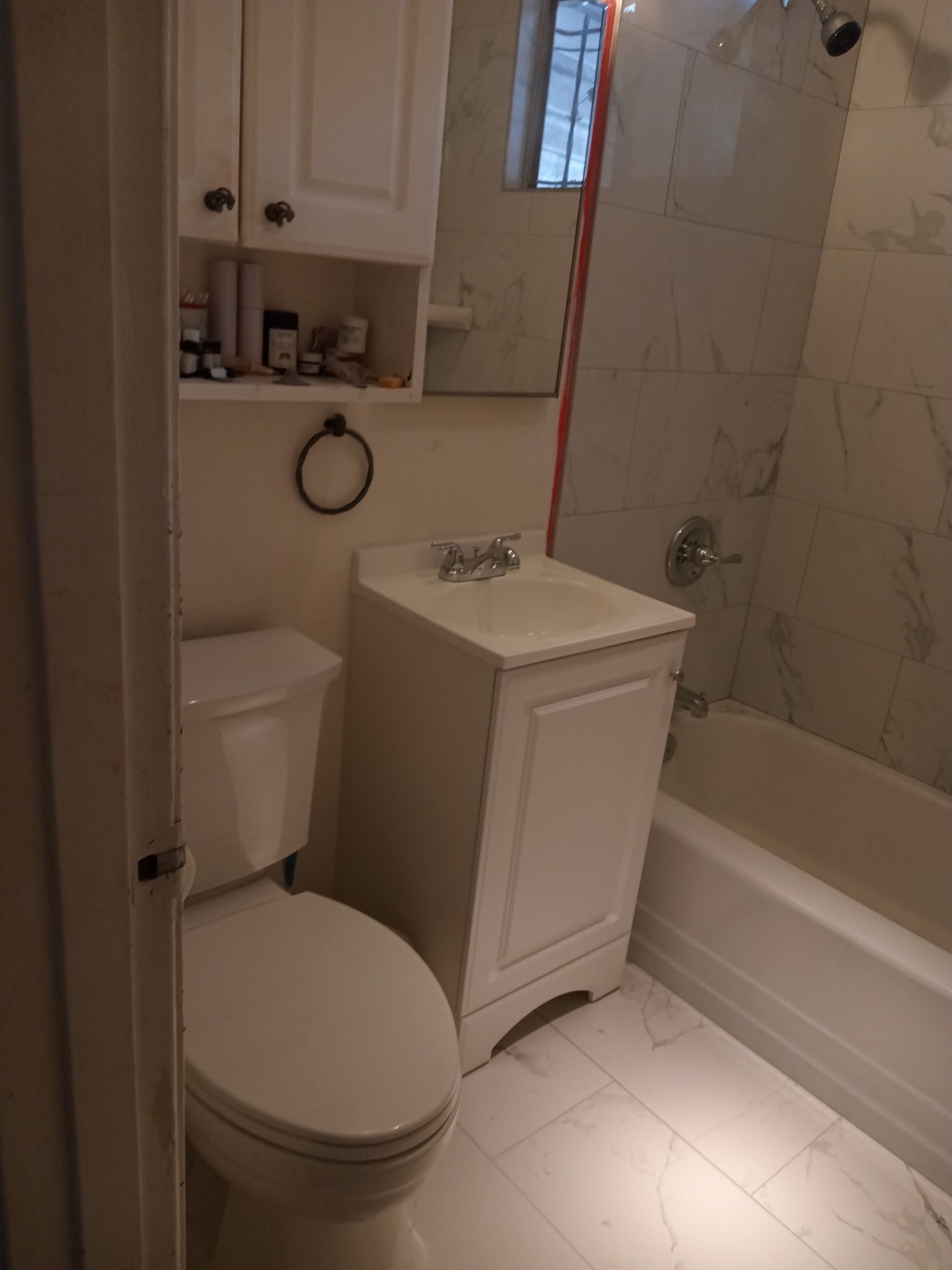 Small bathroom with white toilet, sink, and bathtub. White tiled walls and floor.